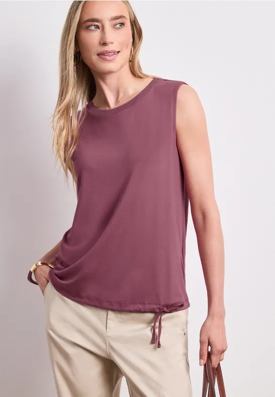 Model trägt ärmelloses, violettes Top mit Kordelzugbund und beige Hose.