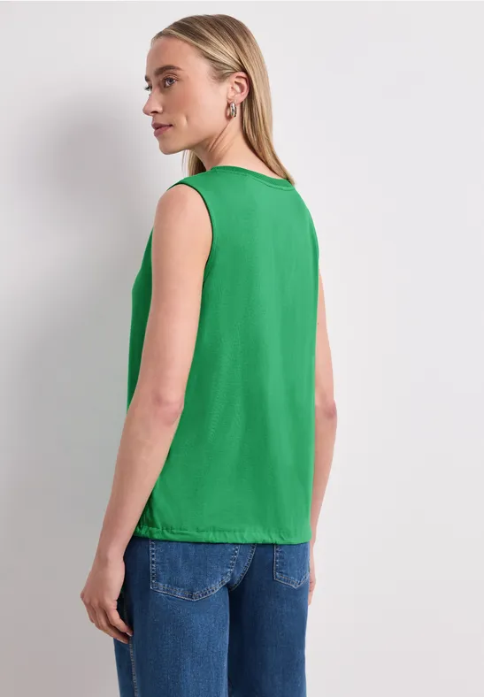 Frau zeigt Rücken, trägt grünes ärmelloses Top und blaue Jeans.