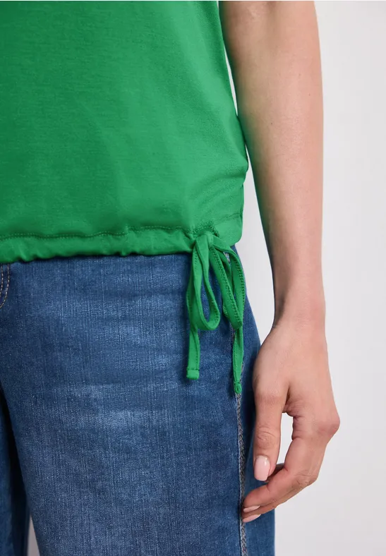 Teilansicht einer Person in grünem Top und Jeans mit sichtbarer Hand am Oberschenkel.