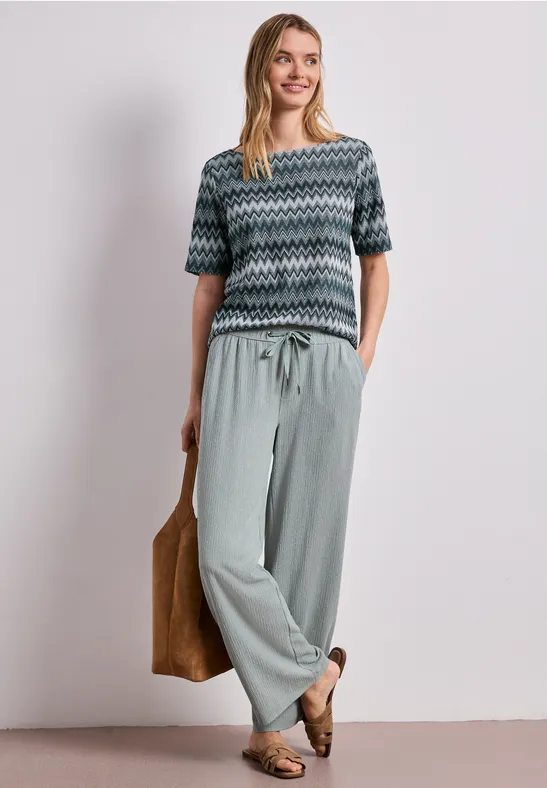 Vrouw in een gebreid shirt met zigzagmotief en losse broek, casual met tas en loafers.