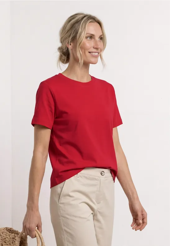 Persoon in rood T-shirt en beige broek voor een witte achtergrond, gezicht onscherp.