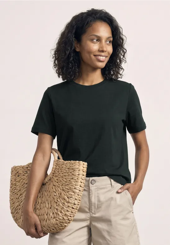 Vrouw in zwart T-shirt en beige broek met een grote gevlochten strotas.