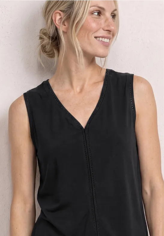 Frau mit hochgesteckten Haaren trägt ein ärmelloses schwarzes Top mit V-Ausschnitt vor hellem Hintergrund.