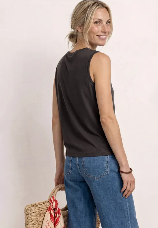 Frau von hinten, trägt schwarzes ärmelloses Top, blaue Jeans und hält eine geflochtene Tasche.