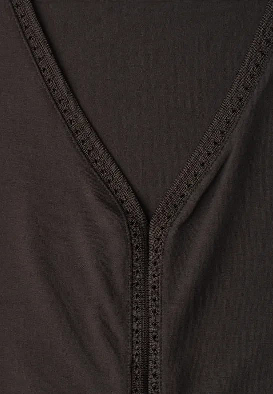 Nahaufnahme eines schwarzen V-Ausschnitt-Oberteils mit feiner Lochverzierung am Kragen.