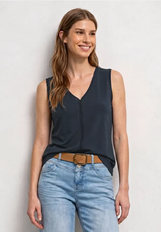 Een vrouw draagt een donkerblauw mouwloos topje, een lichte spijkerbroek en een bruine riem.