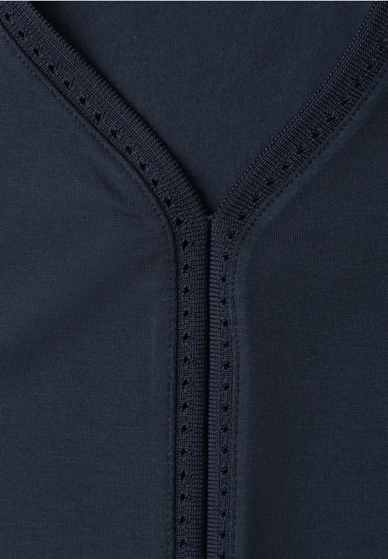 Close-up van donkerblauwe stof met V-vormige naad en fijne siergaatjes.