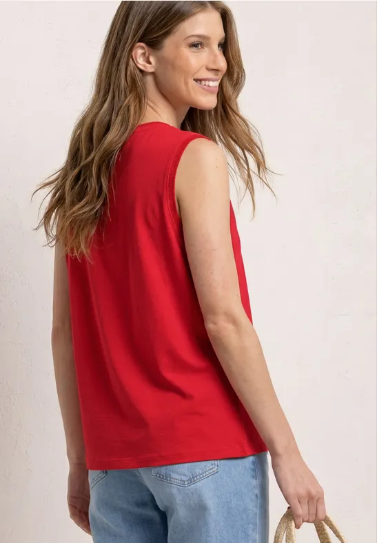 Vrouw van achteren in rood mouwloos topje en blauwe jeans, met een smartphone in haar hand.