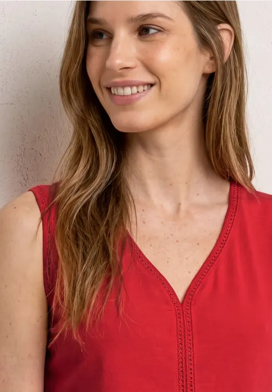 Vrouw met lang haar in een rood mouwloos topje voor een lichte achtergrond.