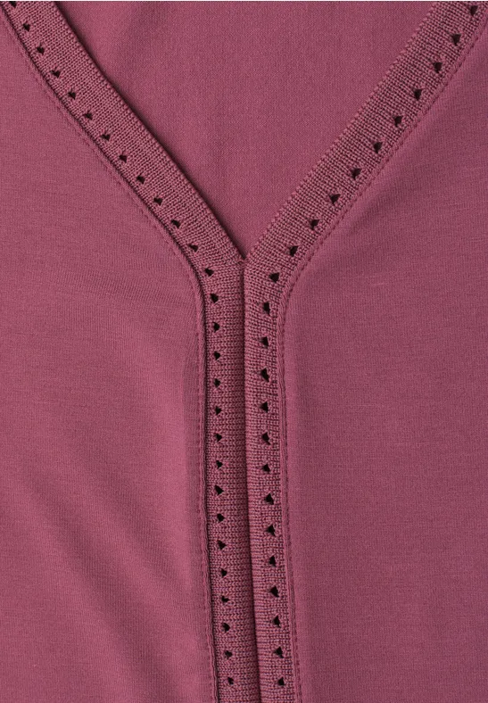 Close-up van een roze top met V-hals en sierlijke oogjesrand