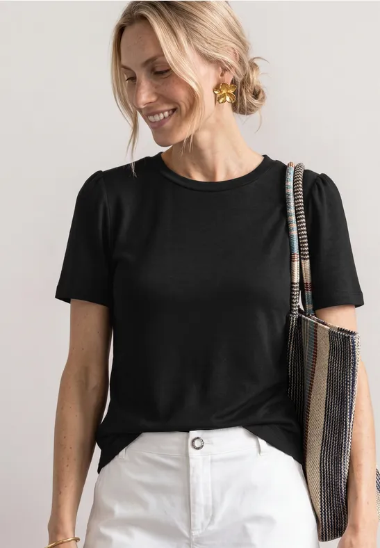 Eine Person in schwarzem T-Shirt und weißen Hosen trägt eine gestreifte Tasche und goldene Ohrringe.