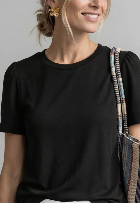 Frau trägt eine hellblaue Jeansjacke mit Knopfleiste über einem grünen Pullover und Schultertasche.