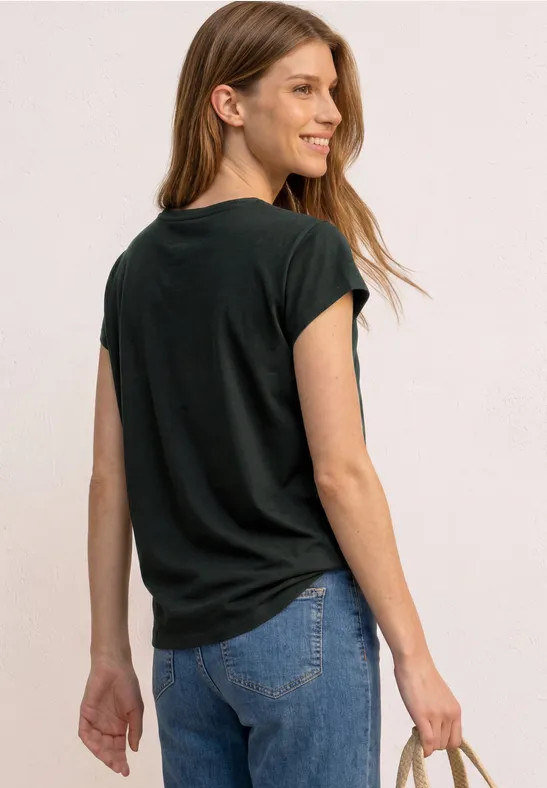 Vrouw gezien van achteren, met een zwart T-shirt, blauwe jeans en een gevlochten tas in de hand.