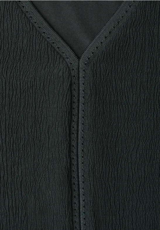 Close-up van een zwart textuurt kledingstuk met V-hals en fijne perforaties langs de rand.