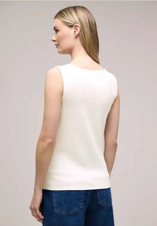 Frau mit blondem Haar, von hinten im weißen, ärmellosen Top und blauen Jeans vor neutralem Hintergrund.