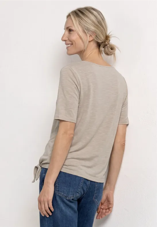 Frau von hinten in beige T-Shirt und blauen Jeans, Haare zu einem lockeren Dutt gebunden.