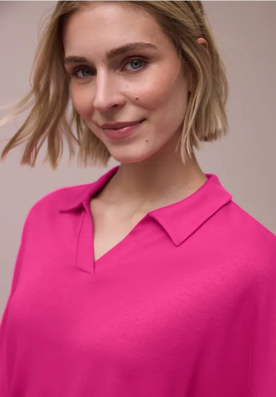 Persoon met felroze poloshirt tegen neutrale achtergrond.