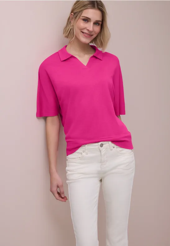 Vrouw met felroze poloshirt en witte spijkerbroek voor beige achtergrond.