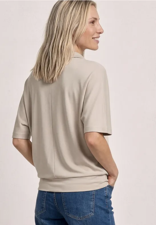 Een persoon gezien van achteren draagt een beige t-shirt en blauwe jeans.