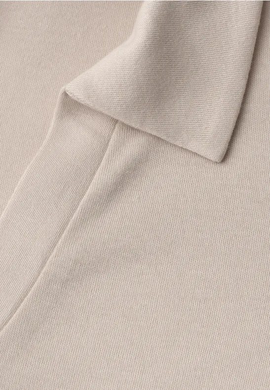 Close-up van een beige gebreide sjaal op een bijpassende gebreide achtergrond.