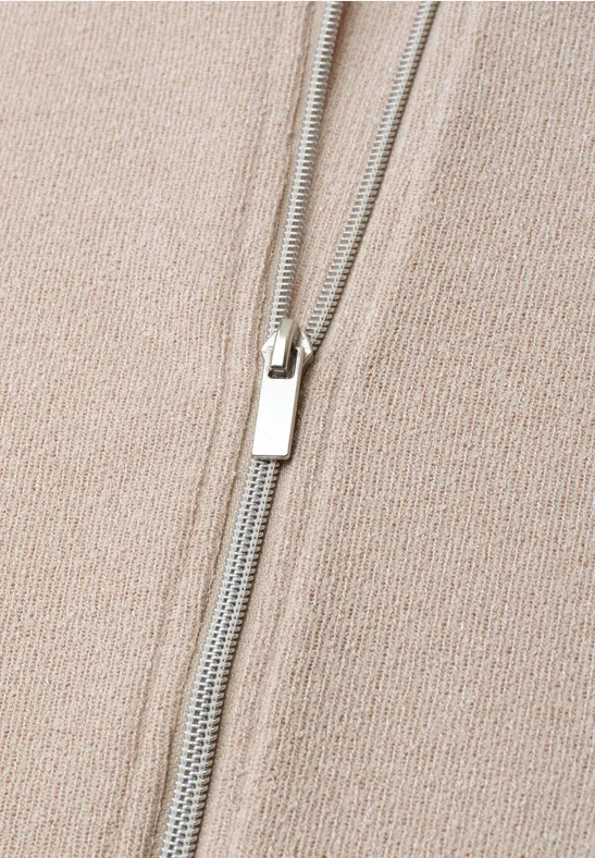 Nahaufnahme eines beigen Strickstoffs mit silbernem Reißverschluss mittig