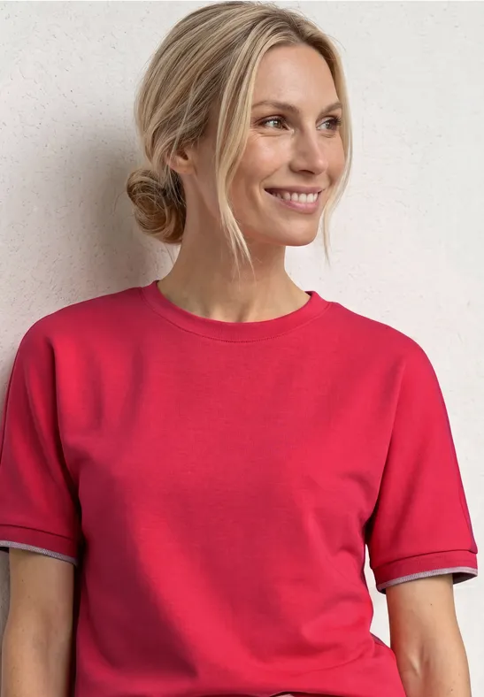 Frau mit hochgestecktem Haar trägt rotes T-Shirt vor hellem Hintergrund.