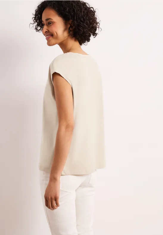 Zijaanzicht van een persoon in een beige top en witte broek.