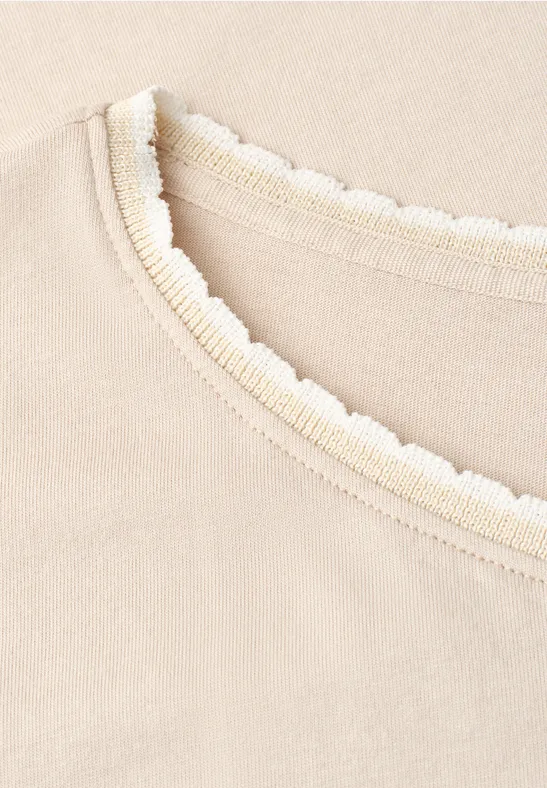 Close-up van beige stof met geribbelde halslijn en golvend kantdetail.