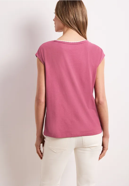 Femme de dos portant un T-shirt rose et un pantalon clair sur fond neutre.