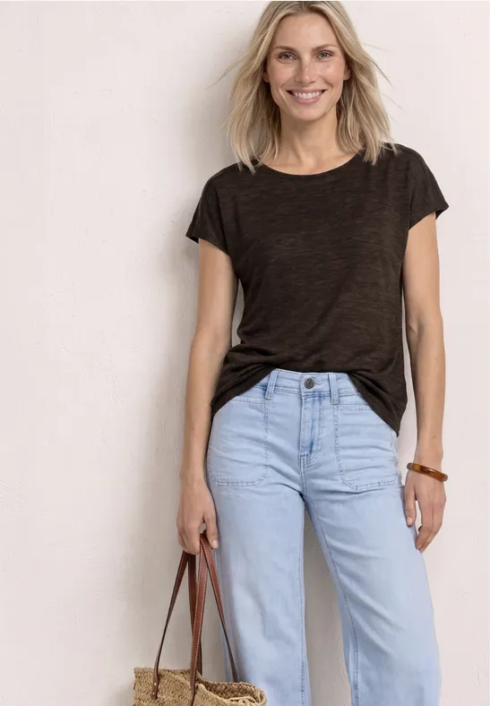 Frau in dunkelgrauem T-Shirt, hellblauen Jeans mit lässiger Tasche vor weißem Hintergrund.