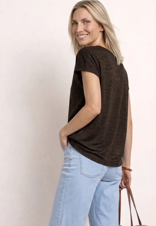 Rückansicht einer Frau in braunem T-Shirt, hellblauer Jeans und Lederhandtasche vor hellem Hintergrund.