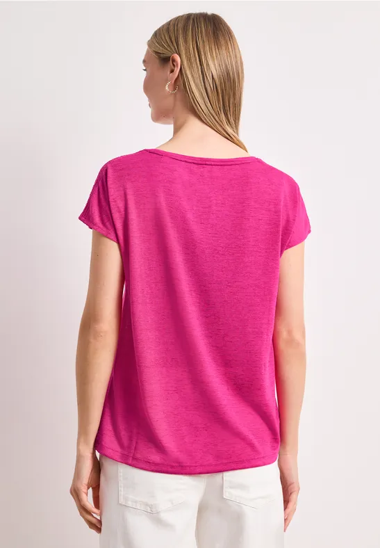 Frau von hinten in pinkem T-Shirt und weißen Hosen vor weißem Hintergrund.