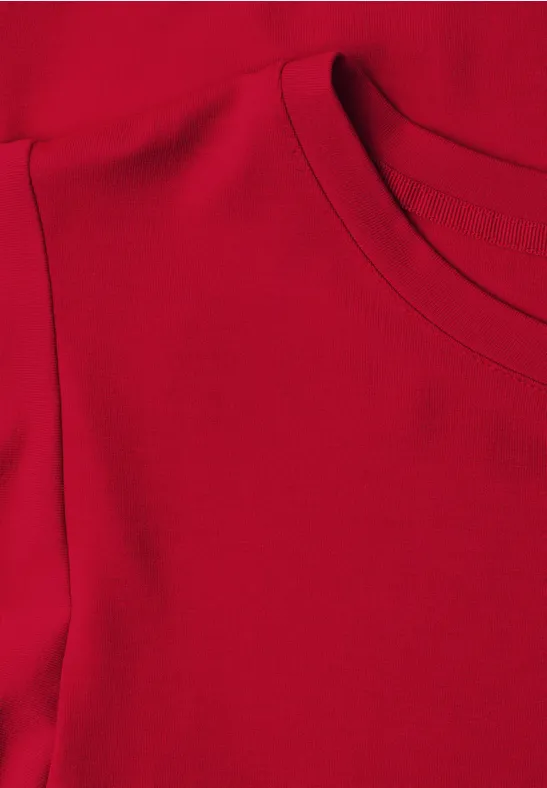 Rotes Textil mit Rundhalsausschnitt und Schulternaht, Detailaufnahme eines Oberteils.