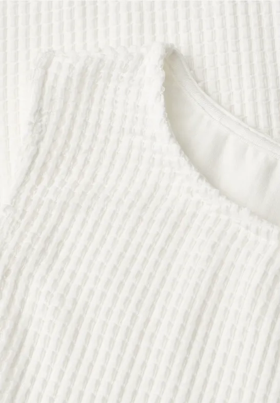 Close-up van witte geribbelde stof met ronde halslijn.