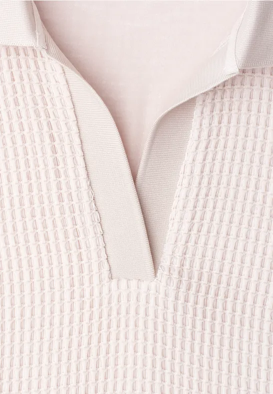 Close-up van een lichtbeige gebreide polo met V-hals en fijne structuur