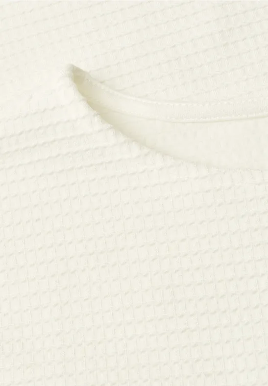 Close-up van een wit kledingstuk met wafelstructuur en ronde halslijn.
