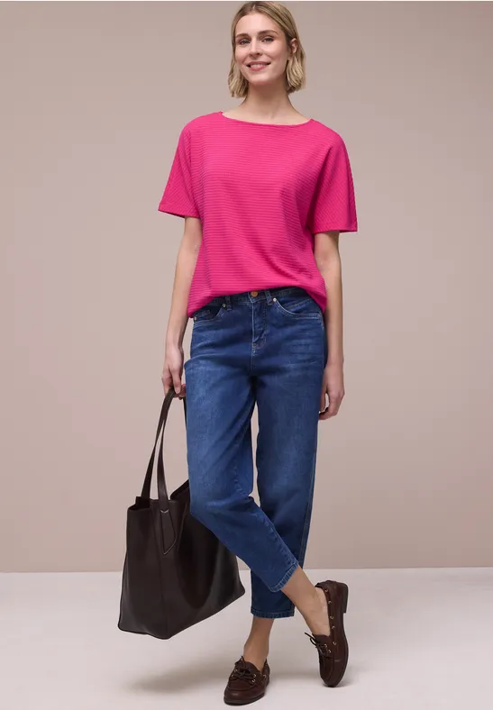 Vrouw in een roze t-shirt, blauwe jeans, bruine loafers en met een grote zwarte tas.