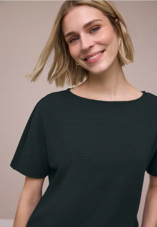 Vrouw met blond haar draagt een zwart, kort mouwshirt voor een neutrale achtergrond.