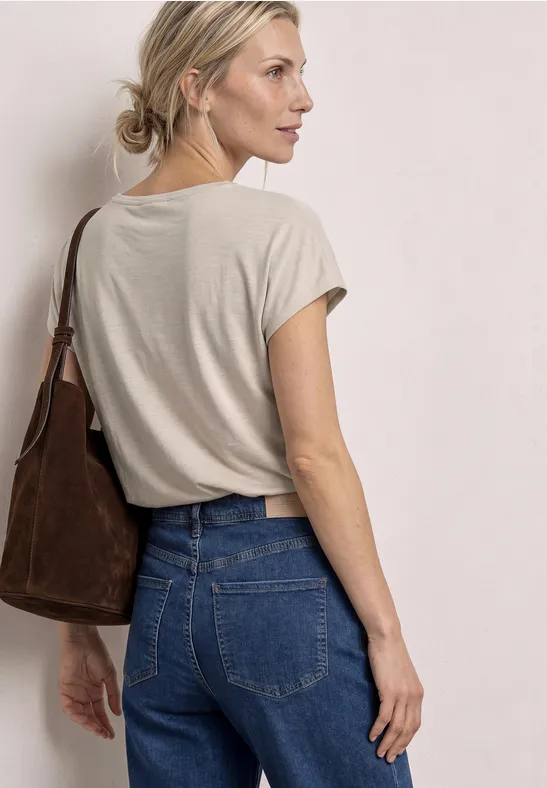 Vrouw van achter gezien met beige T-shirt en spijkerbroek, bruine schoudertas, haar in een knot.