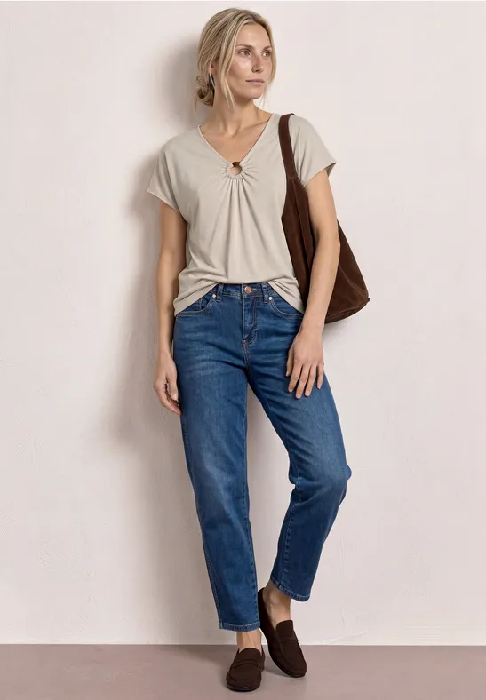 Persoon in wit geknoopt T-shirt, blauwe jeans, bruine schoenen en schoudertas voor lichte achtergrond.