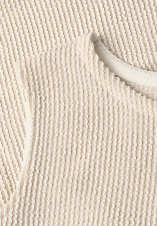 Close-up van een crèmekleurige, geribbelde gebreide top met ronde hals.
