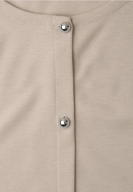 Nahaufnahme eines beigen Kleidungsstücks mit zwei silbernen Druckknöpfen in der Mitte.