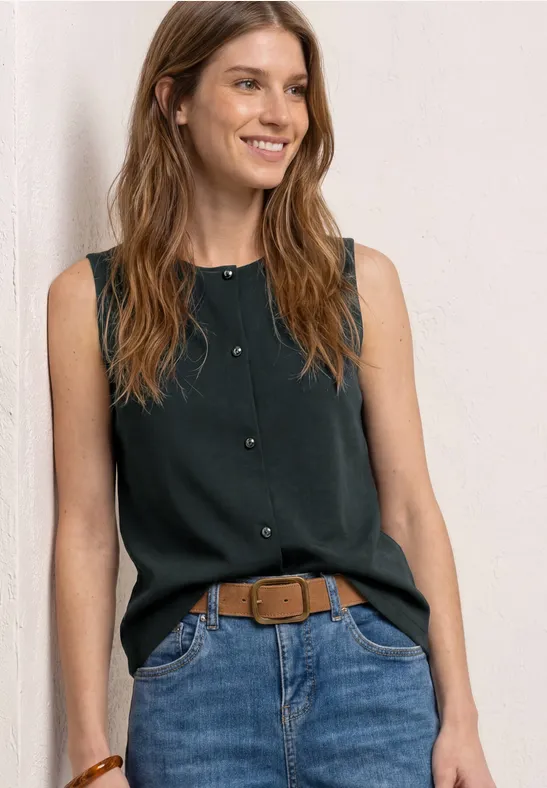 Eine Frau mit langem Haar trägt ein ärmelloses schwarzes Top, blaue Jeans und einen braunen Gürtel.