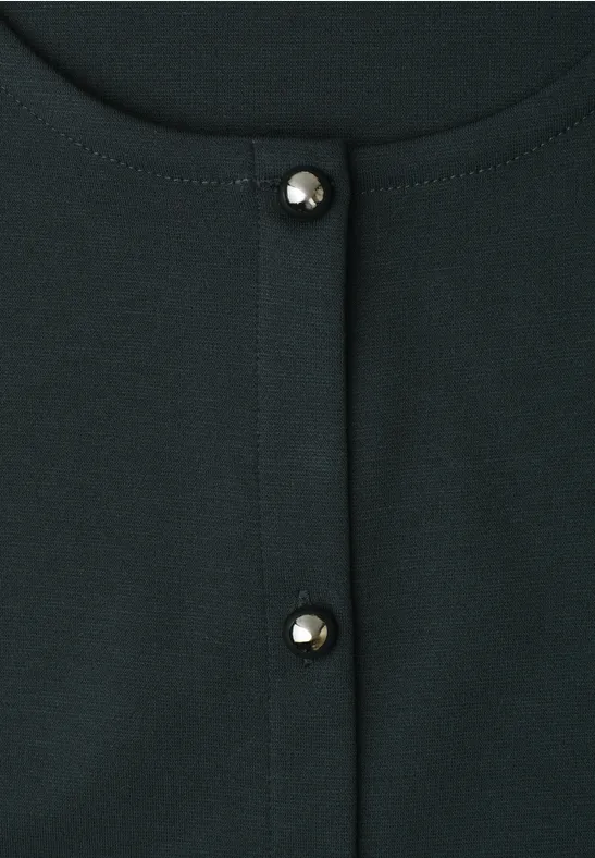 Nahaufnahme eines dunkelgrünen Oberteils mit zwei glänzenden Perlenknöpfen