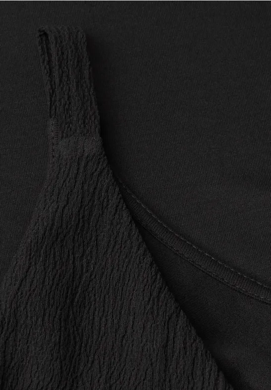 Close-up van een zwart topje met gekreukte textuur.