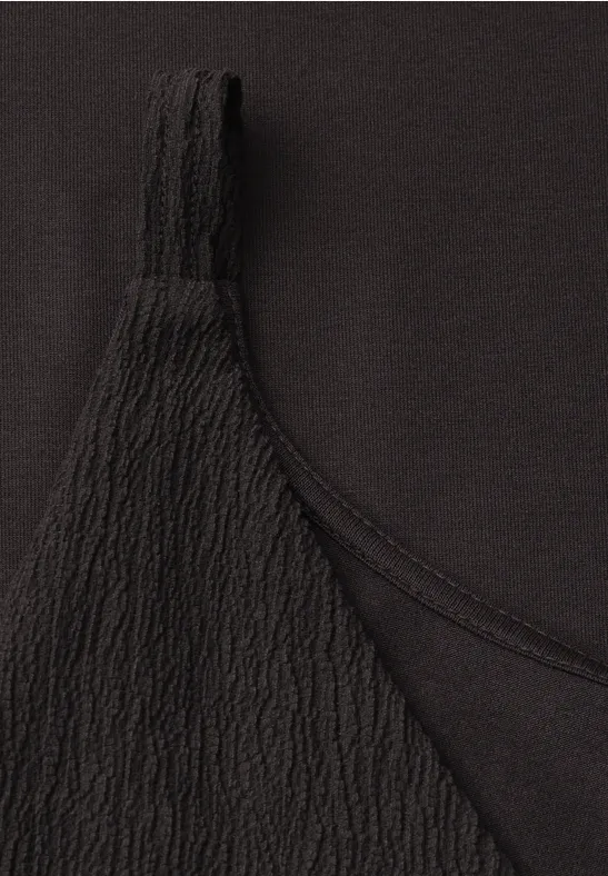 Gros plan sur un haut noir, bretelle texturée avec motif fin sur fond uniforme.