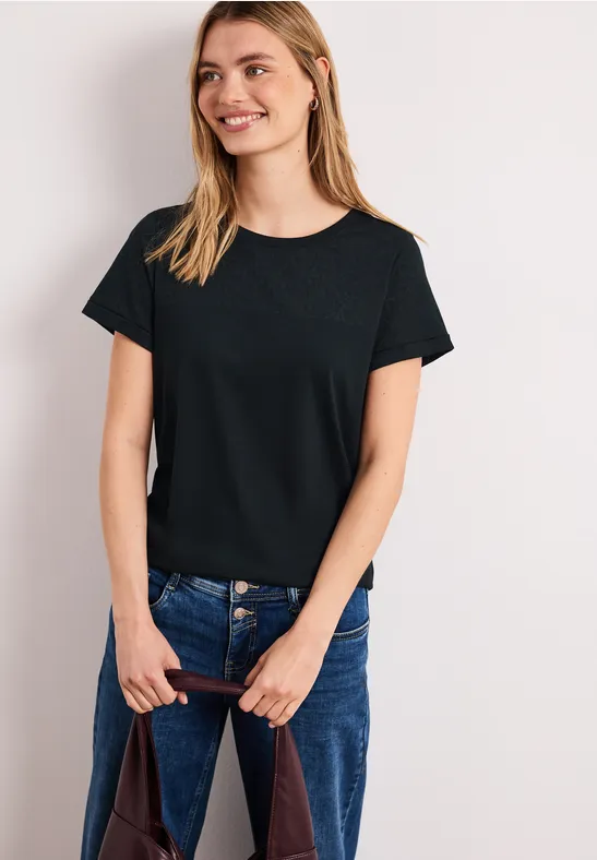 Jonge vrouw in zwart T-shirt en blauwe jeans, met een tas in haar handen.