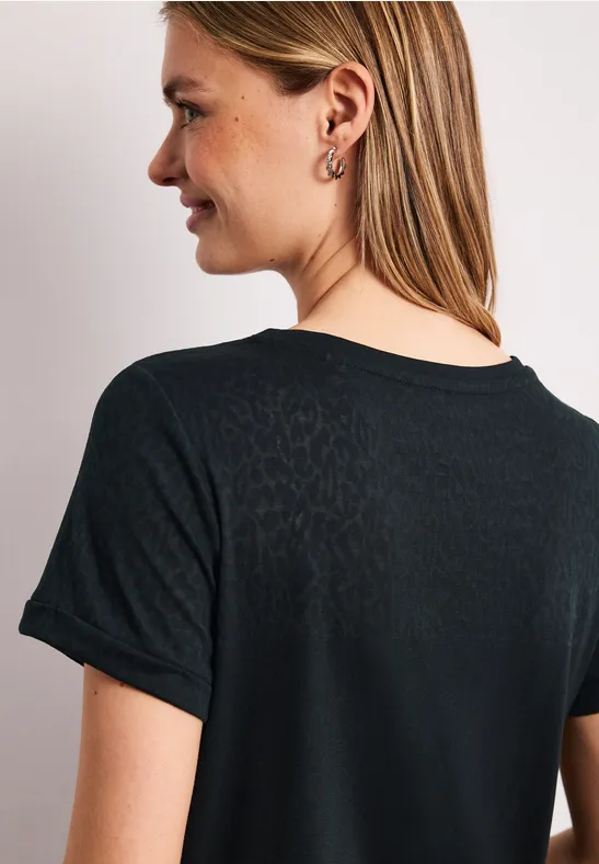 Vrouw van achteren in zwart T-shirt met korte mouwen, halflang blond haar, tegen een witte achtergrond.