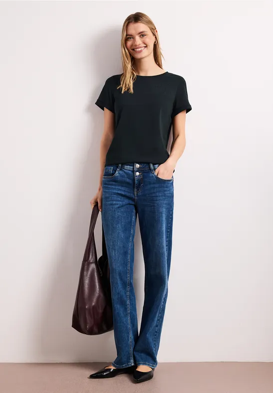 Persoon in zwart T-shirt, blauwe jeans en zwarte ballerina's, met een bruine tas.