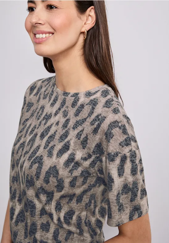 Frau in grauem Pullover mit dunklem Leopardenmuster vor hellem Hintergrund.